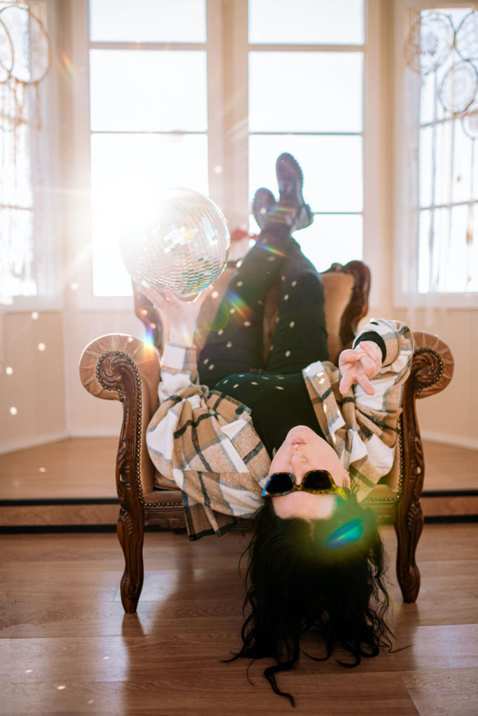 branding photo of a woman upside down in a chair holding a disco ball inside Big Love Tiny Chapel